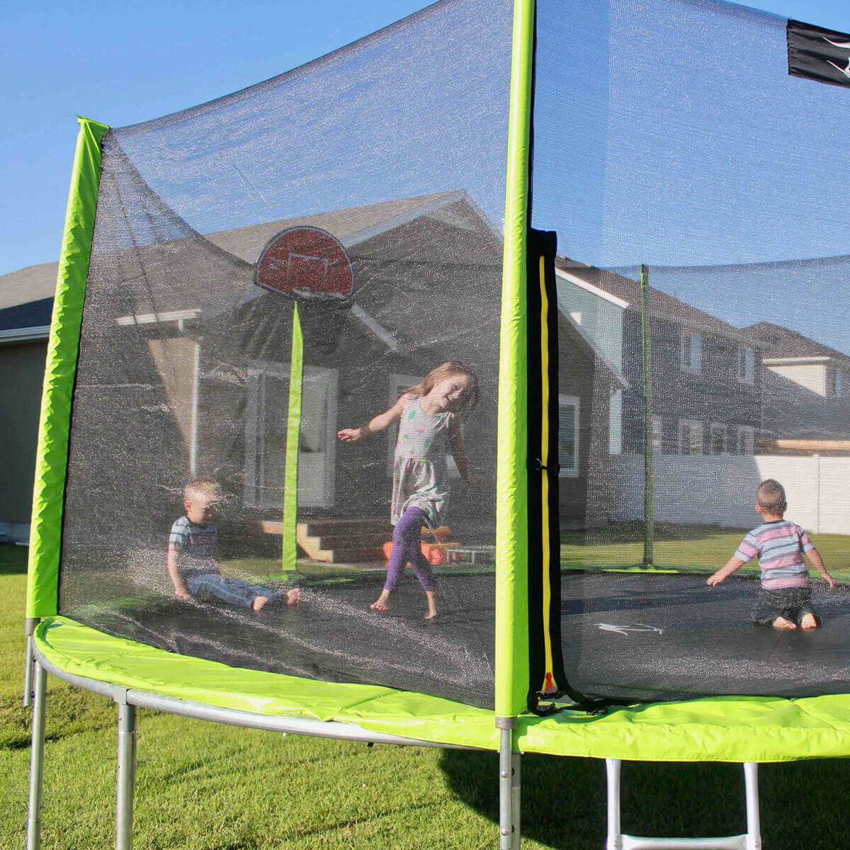 Children jumping on agreen trampoline with a safety net and basketball hoop