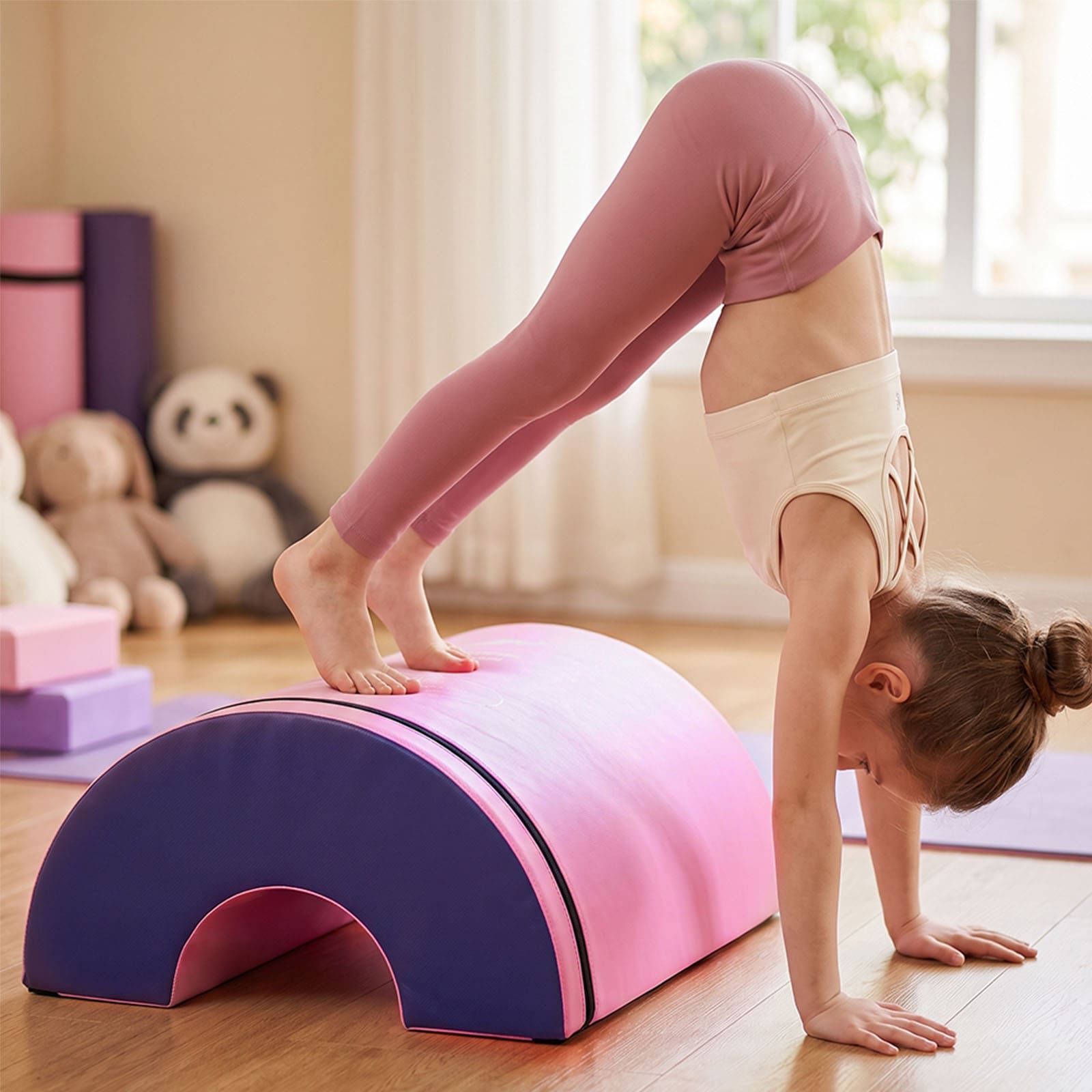 A child in pink leggings and a white tank top performs a handstand on a pink and purple 4-in-1 Modular Training System in a bright indoor room with wooden floors and stuffed animals in the background.